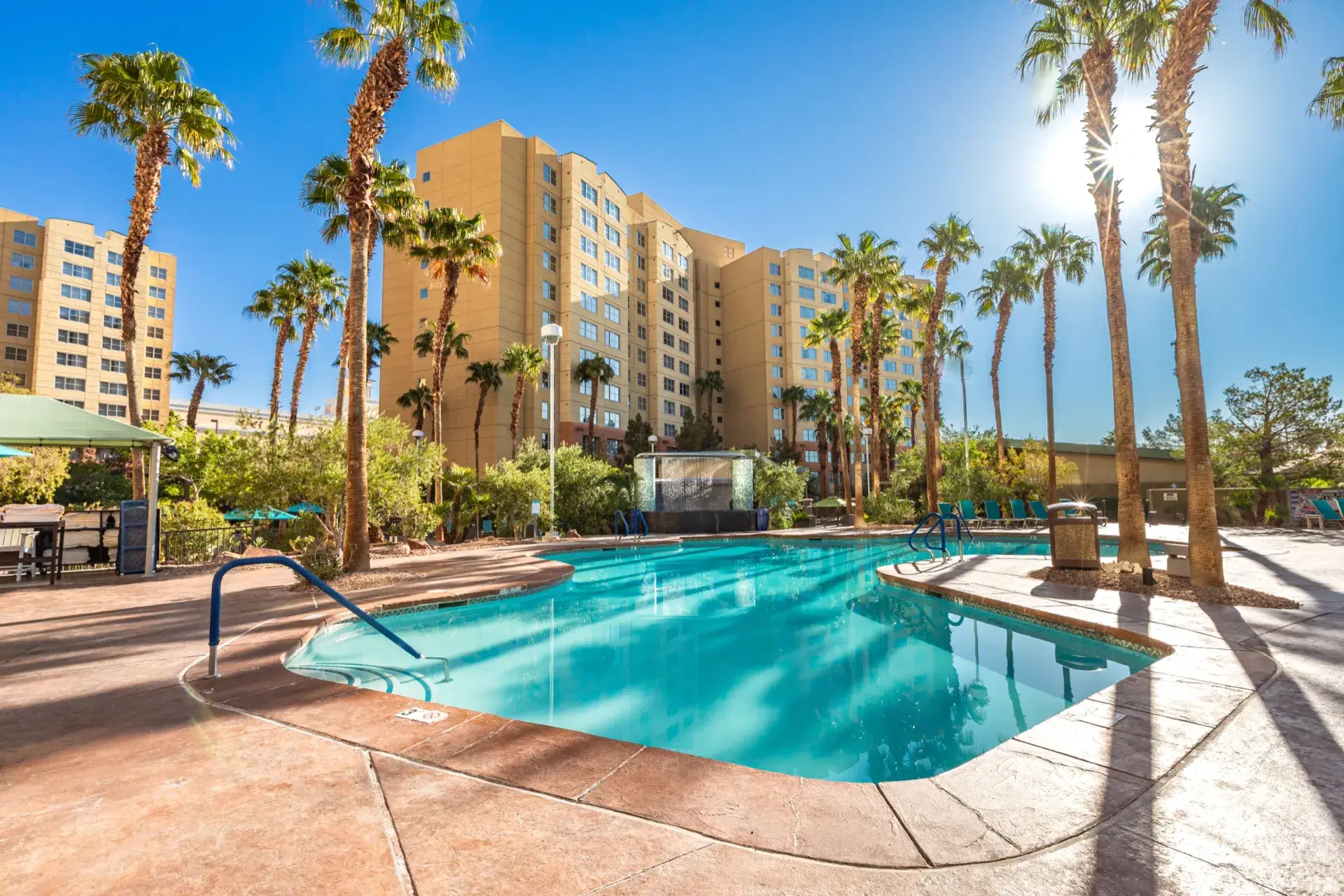 Una piscina al aire libre iluminada por el sol, rodeada de palmeras y edificios del resort en Grandview at Las Vegas